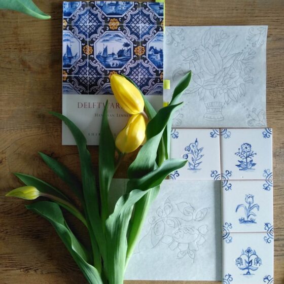 Kafle Delft, projekty i gotowe mini-kafle leżące na stole z żółtymi tulipanami