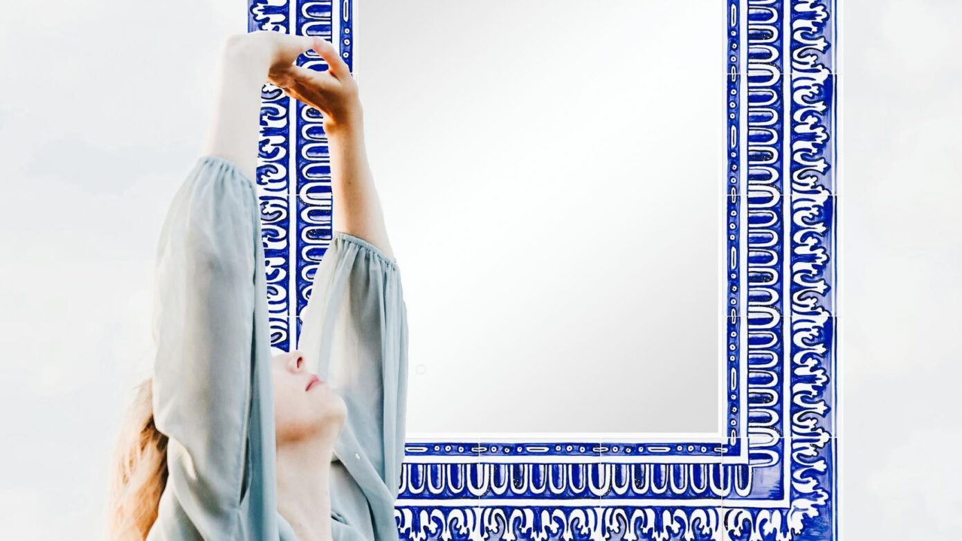 kobieta w zwiewnej sukni przeciągająca się przed lustrem o malowanej ramie z kafli ceramicznych - tak mogą wyglądać poranki jeśli zadbasz o lustro w łazience