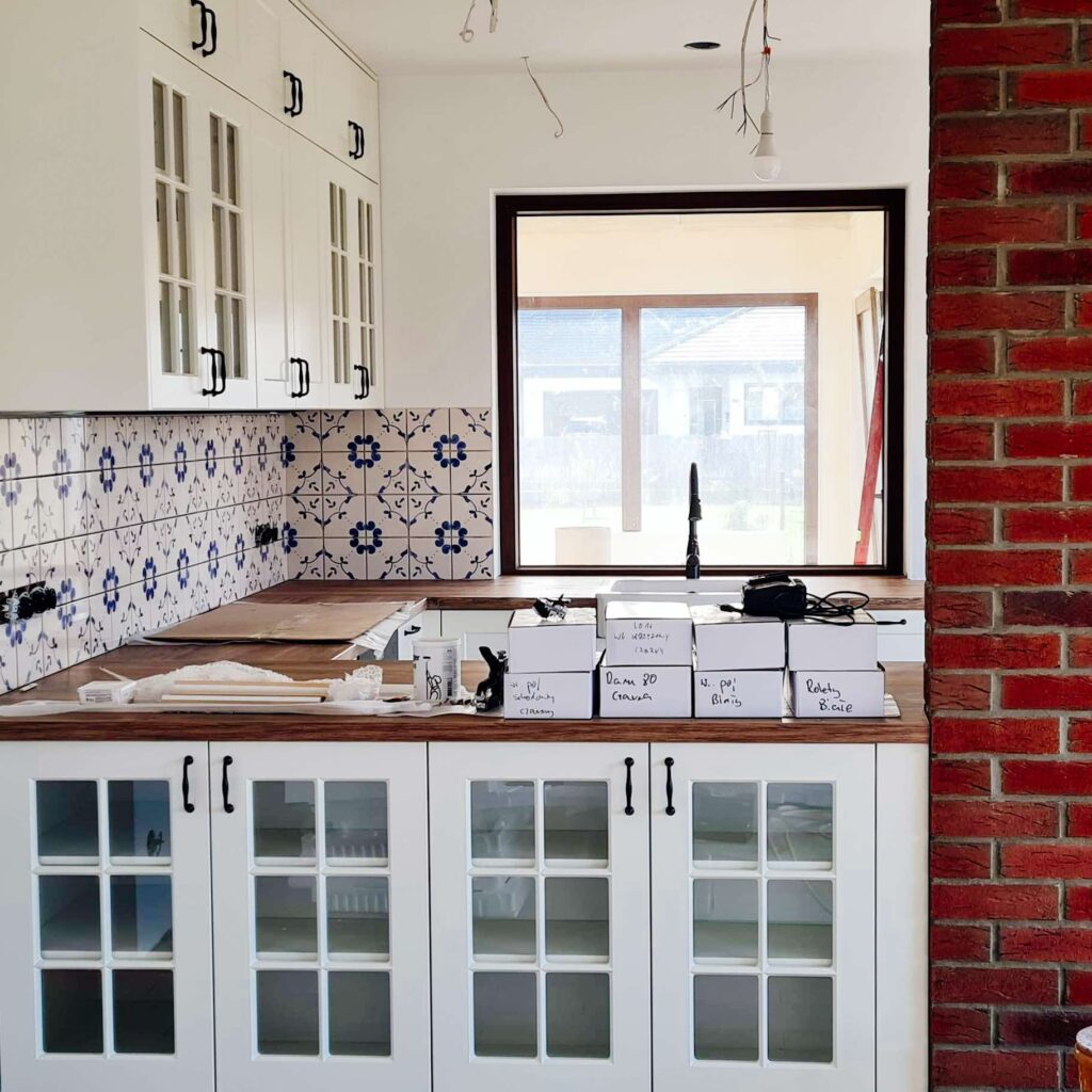 Kuchnia z białą zabudową, cegłą i kafelkami ręcznie malowanymi