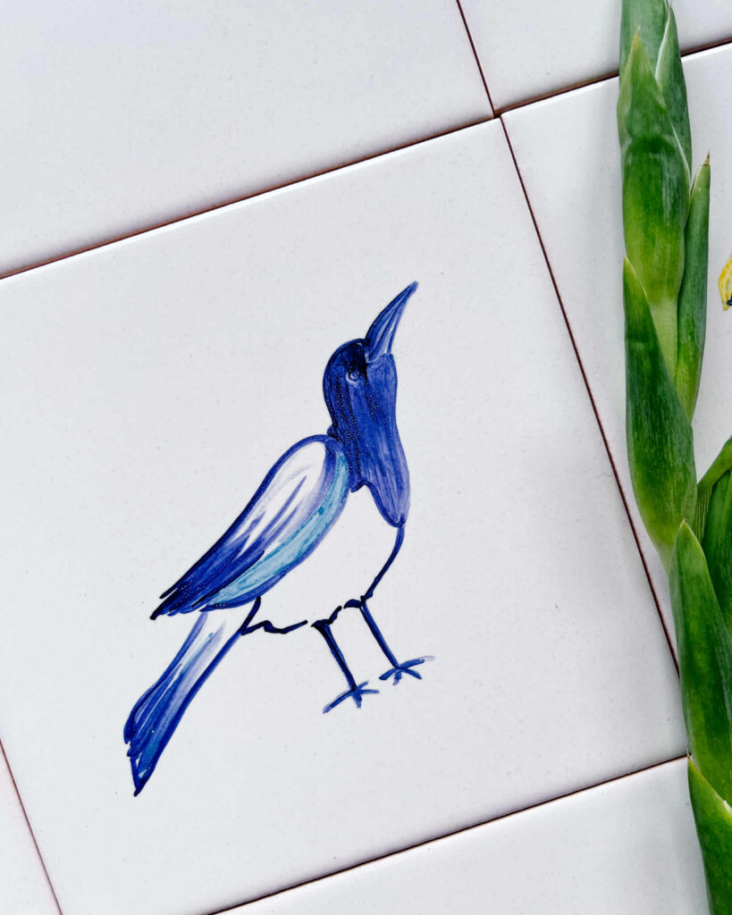 Płytka z ręcznie namalowaną sroką, kolorowa i idealnie do niej pasujące białe płytki