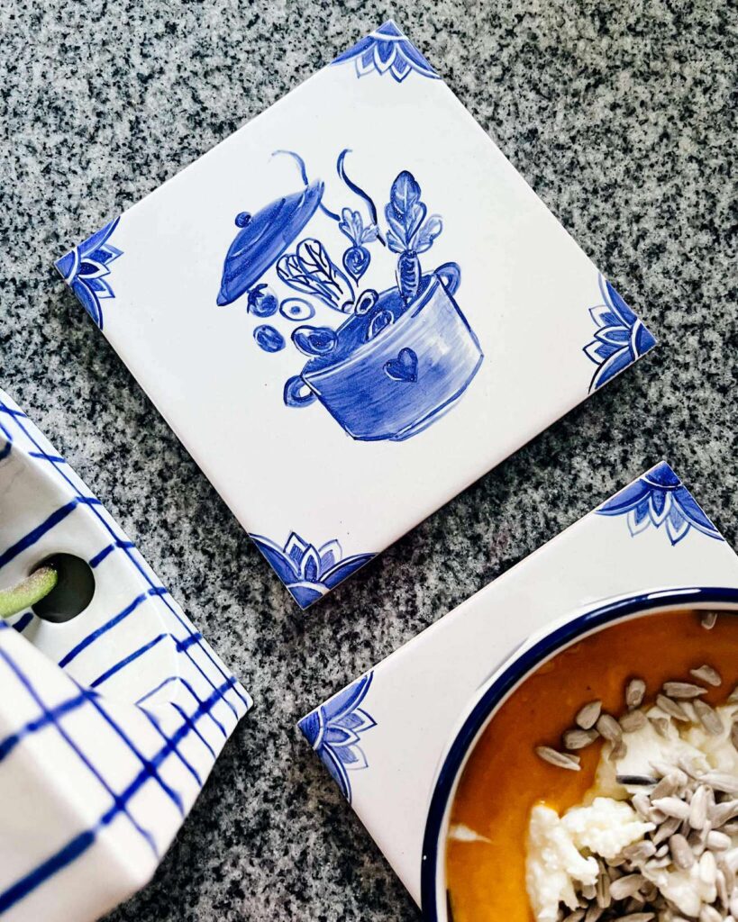Podkładka pod talerz z kafelka ceramicznego z ręcznie malowanym wzorem niebieskim na białym tle przedstawiającym garnek i wrzucane do niego warzywa
