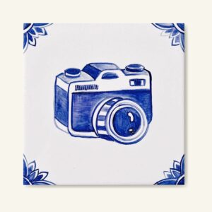 Kafelek ceramiczny z ręcznie malowanym wzorem niebieskim na białym tle przedstawiający aparat fotograficzny (bez oznaczenia marki aparatu)