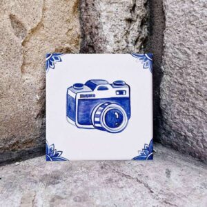 Kafelek ceramiczny z ręcznie malowanym wzorem niebieskim na białym tle przedstawiający aparat fotograficzny (bez oznaczenia marki aparatu)