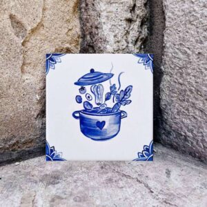 Kafelek ceramiczny z ręcznie malowanym wzorem niebieskim na białym tle przedstawiającym garnek i wrzucane do niego warzywa