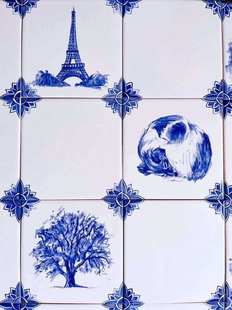 Miks biało-niebieskich wzorów kafli ceramicznych - połowa jest z dekoracjami w samych rogach, a na pozostałych - zwinięty w kłębek pies, orzech włoski (całe drzewo) i wieża Eiffela