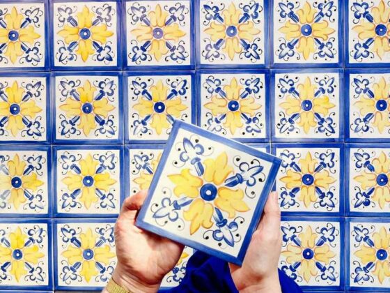 Żółto-niebieski nasycony ornament namalowany ręcznie na kafelkach ceramicznych, jedna sztuja trzymana w rękach autorki