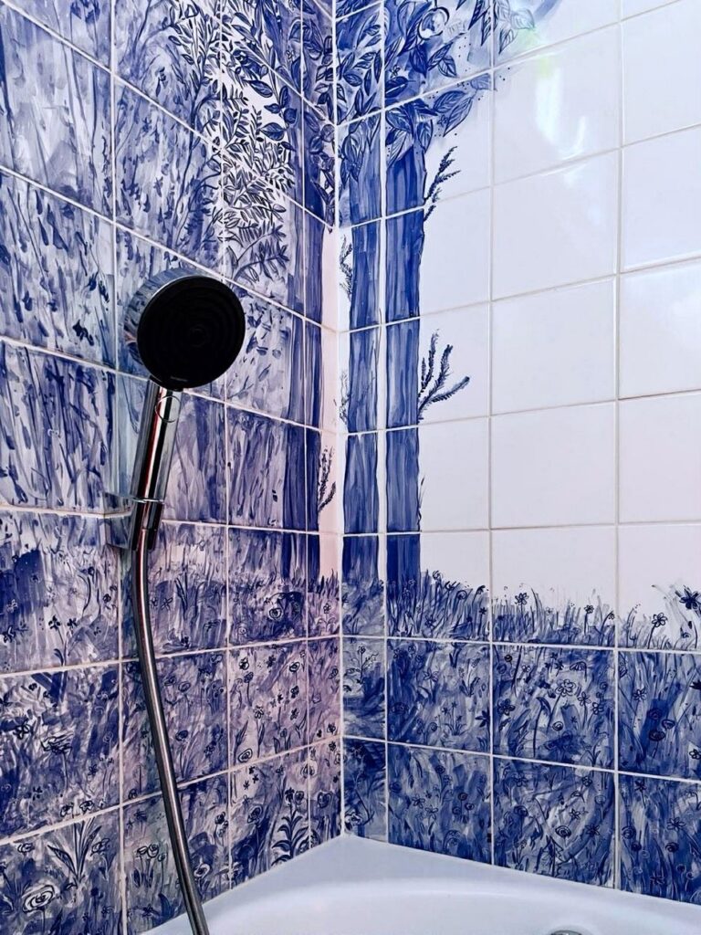 Niebieski we wnętrzach świetnie sprawdzi się zwłaszcza w łazience, dekoracja malowana na płytkach ręcznie, niebieska, nad wanną