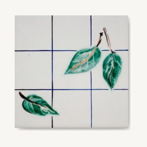 Ręcznie malowany kafelek ceramiczny z motywem zielonych liści na tle niebieskiej kratki.