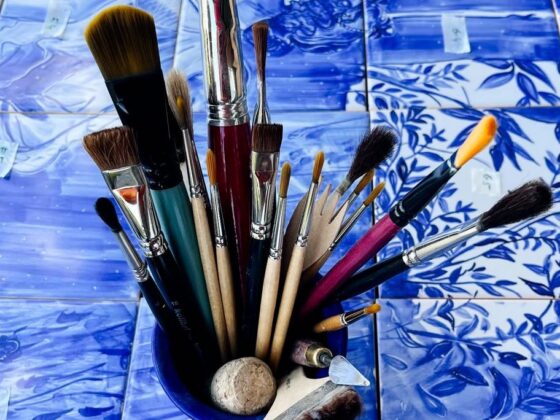 Płytki malowane ręcznie - panel ceramiczny rozłożony na stole, a na nim zestaw pędzli używanych do jego namalowania